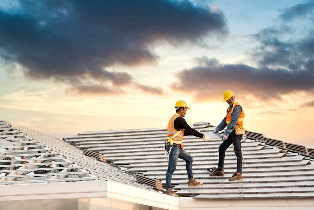 Two workers cover a residential roof with a large tarp during a home renovation project.