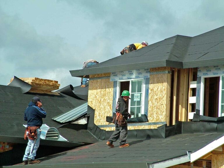A person using a garden hose to gently rinse stains from an asphalt shingle roof on a residential home.