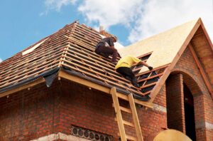 Roof shingles with uneven rows, exposed flashing, and water stains visible inside an attic.