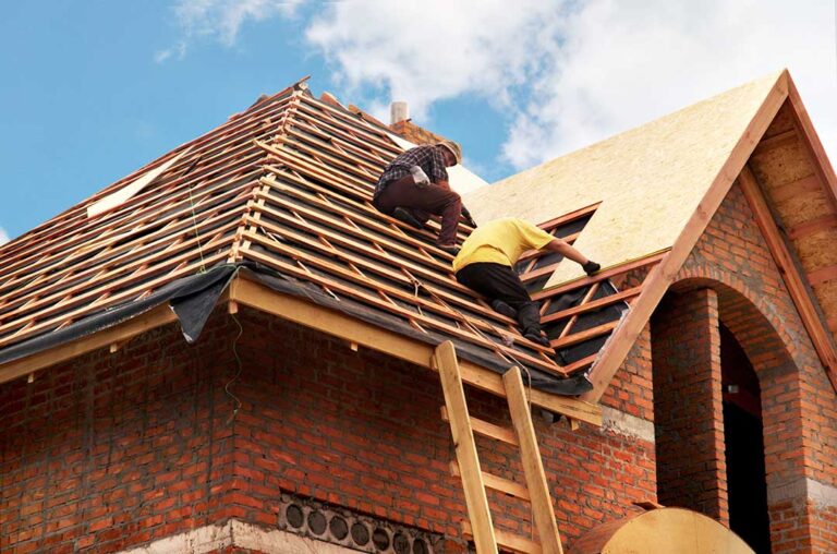 Roof shingles with uneven rows, exposed flashing, and water stains visible inside an attic.